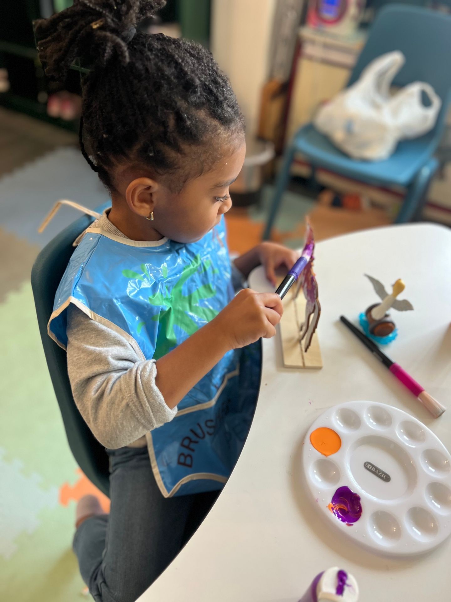 Child painting a wooden figure at a table with a paint palette and brush.