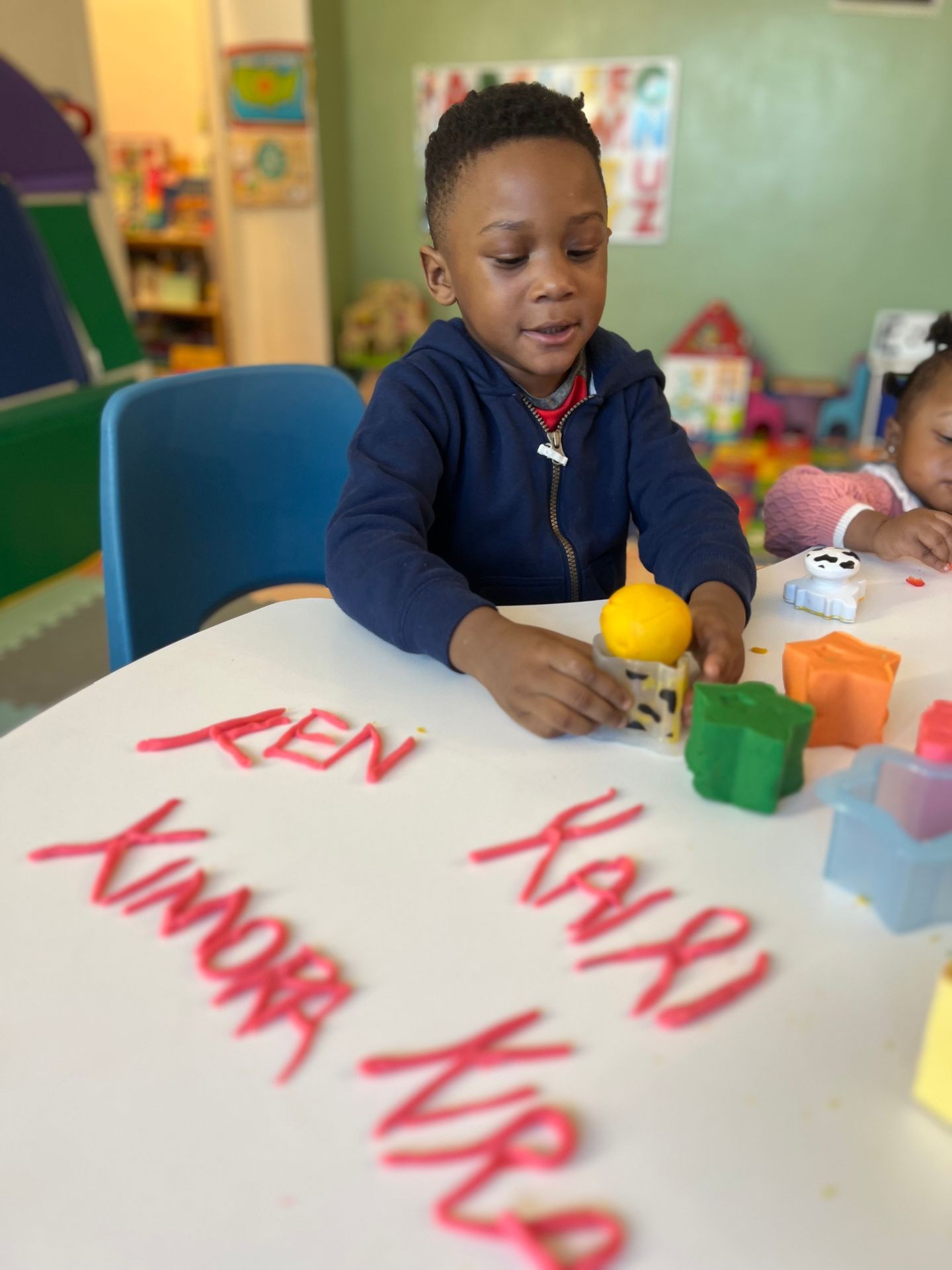 Young child playing with colorful shapes at a table in a classroom setting.
