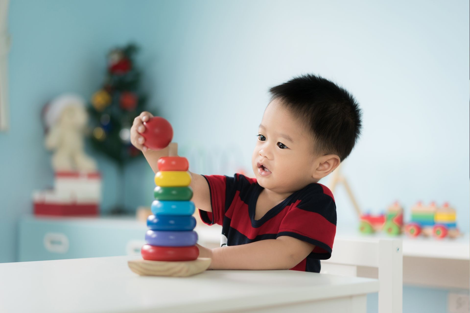 Adorable Asian Toddler baby boy sitting on chair and playing with color developmental toys at home.
